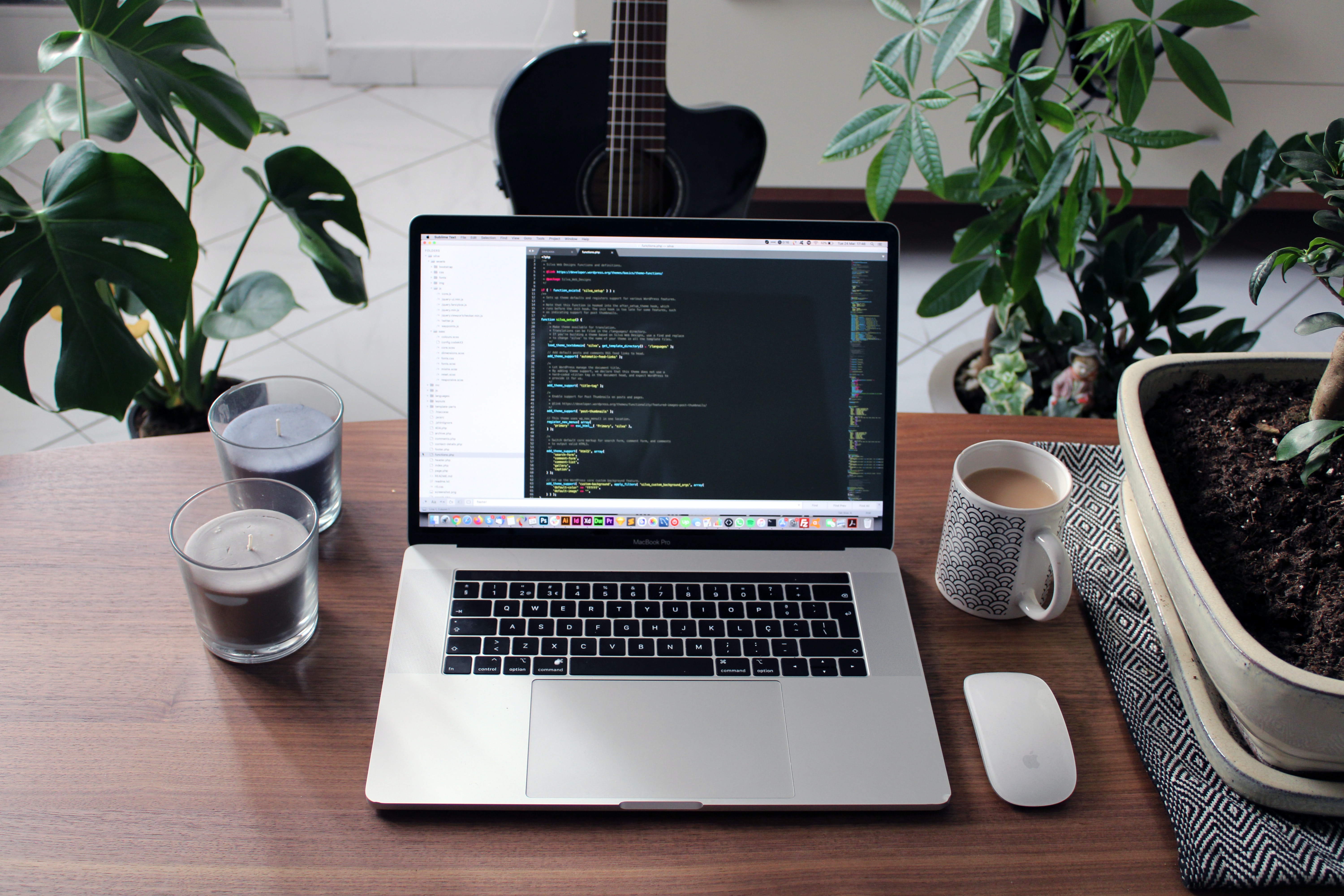 A MacBook on a wooden table displaying code in an IDE, with a focus on implementing best practices for decoupling software using plugins, flanked by indoor plants and a guitar, suggesting a comfortable development environment.