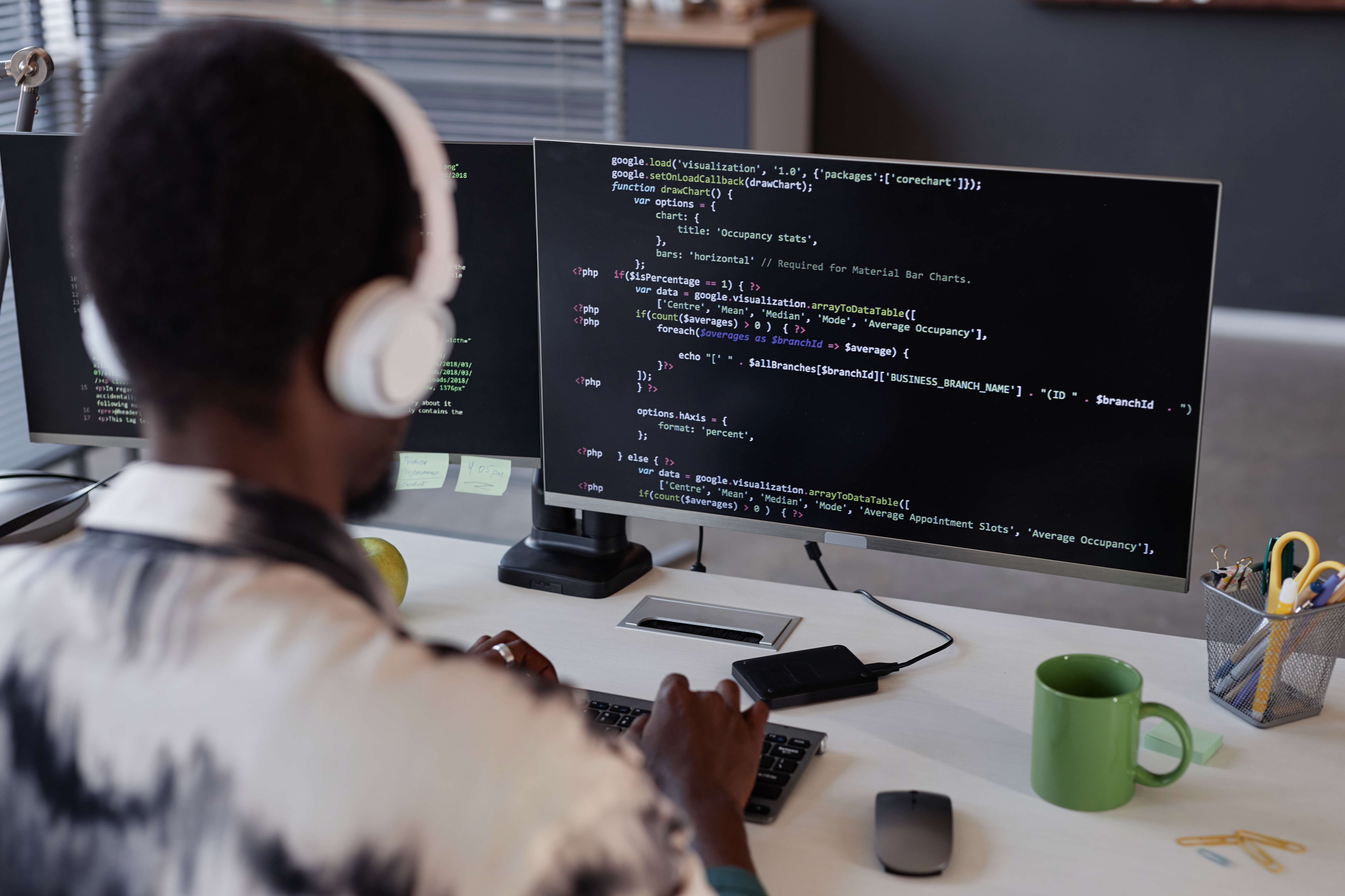 A programmer working on dual monitors while writing code related to Python descriptors for property management and attribute access in a modern office environment.