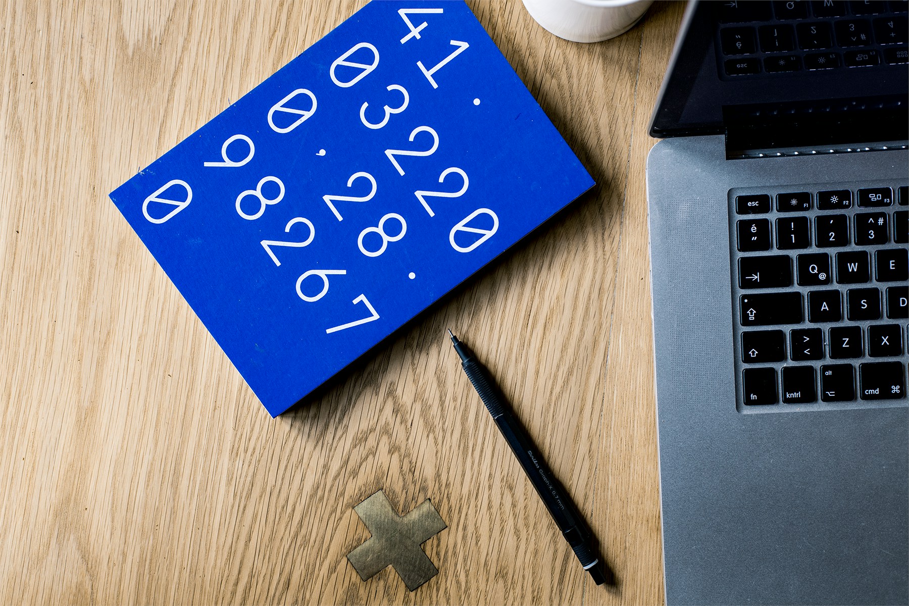 A laptop, pen, and a blue notebook with numbers on a wooden desk, illustrating Python enum classes for managing constants effectively in programming.