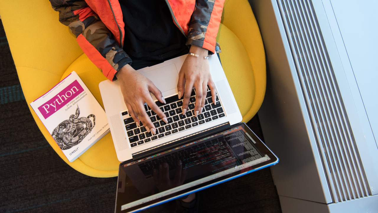 A person typing on a laptop with a Python programming book beside them, symbolizing the concept of understanding Python metaclasses for advanced class customization.